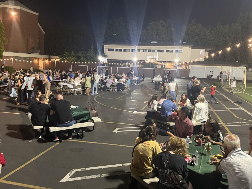 Guests dining at tables on the blacktop under string lights
