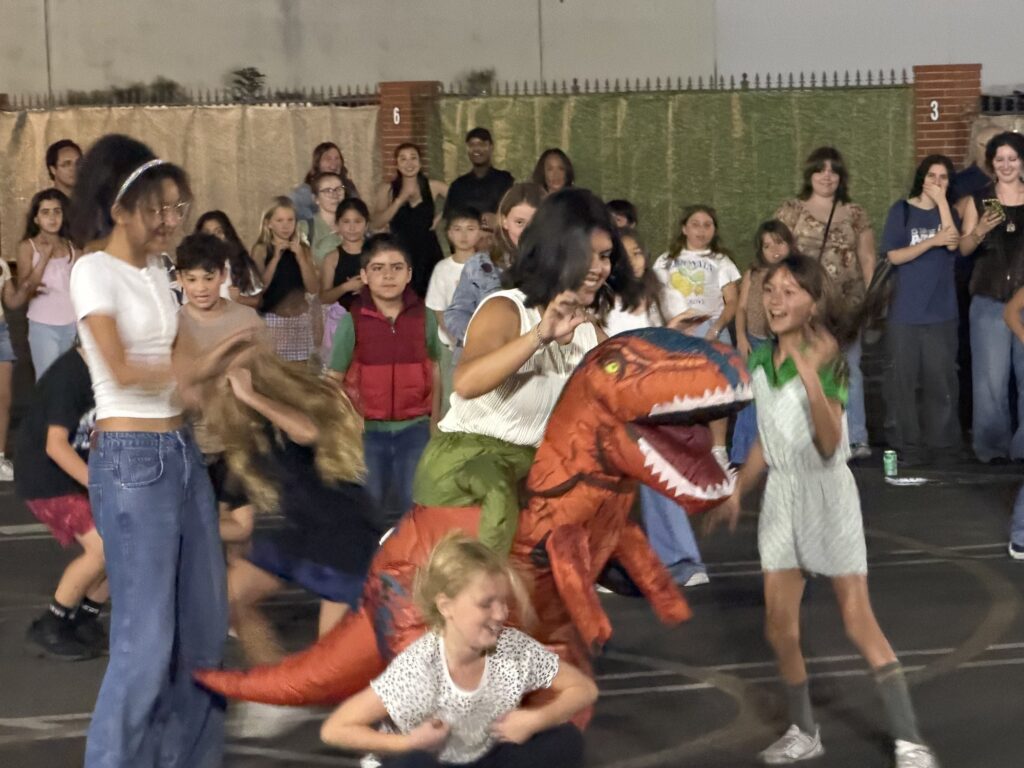 Kids laughing and running from a friend in an inflatable dinosaur costume