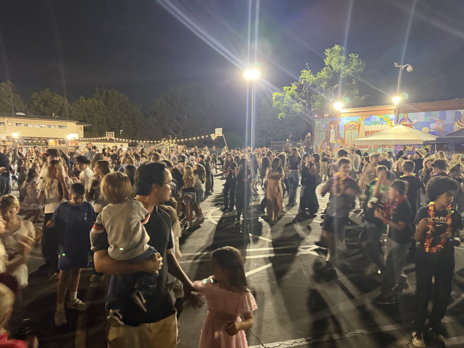 A big crowd of families dancing at night under the lights