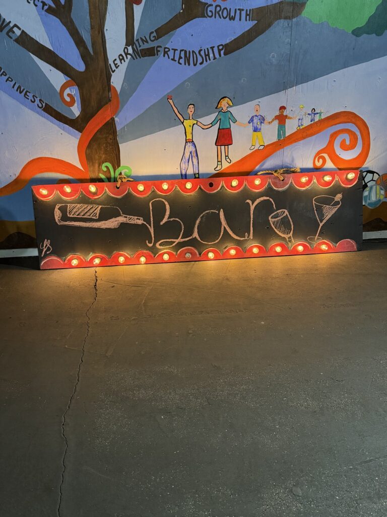 Hand-painted, lit-up bar sign in front of the school mural
