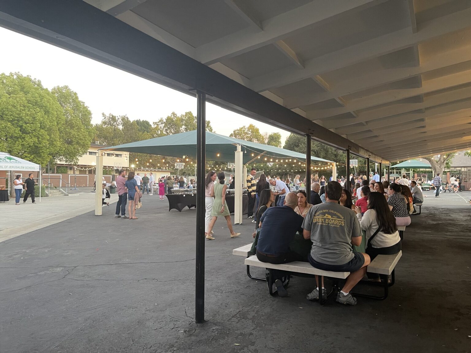 Families gathering at tables under the pavilion string lights